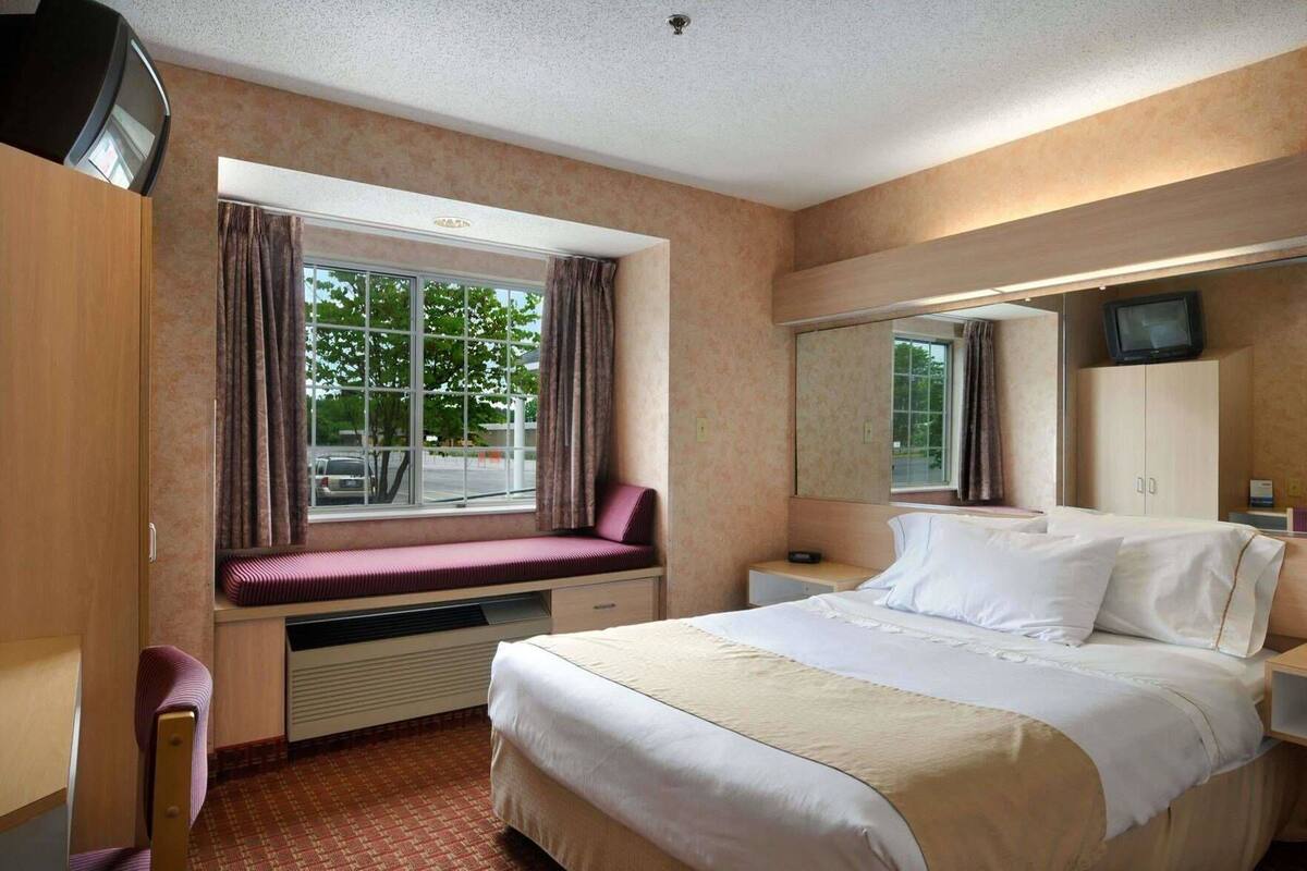 A hotel room with a bed, a window with curtains, a desk, a television, and a mirror.