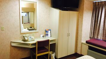 A hotel room with a bed, a desk with a chair, a television, a mirror, and a wardrobe.