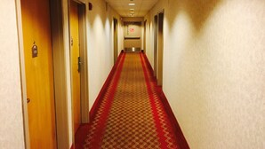 Un couloir d’hôtel avec un tapis rouge, des portes de chaque côté et un panneau sur le mur.