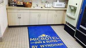 Une cuisine avec des meubles de couleur claire, un four à micro-ondes, un distributeur d’eau et un tapis bleu sur lequel est inscrit « MICROTEL INN & SUITES BY WYNDHAM ».
