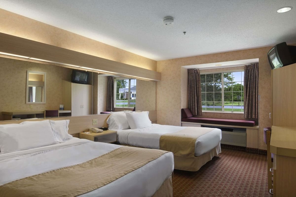 A hotel room with two beds, a large window, a television on a stand, and a mirror on the wall.