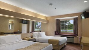 Une chambre d’hôtel avec deux lits, une grande fenêtre avec des rideaux, un téléviseur fixé au mur et un miroir au-dessus du lit.