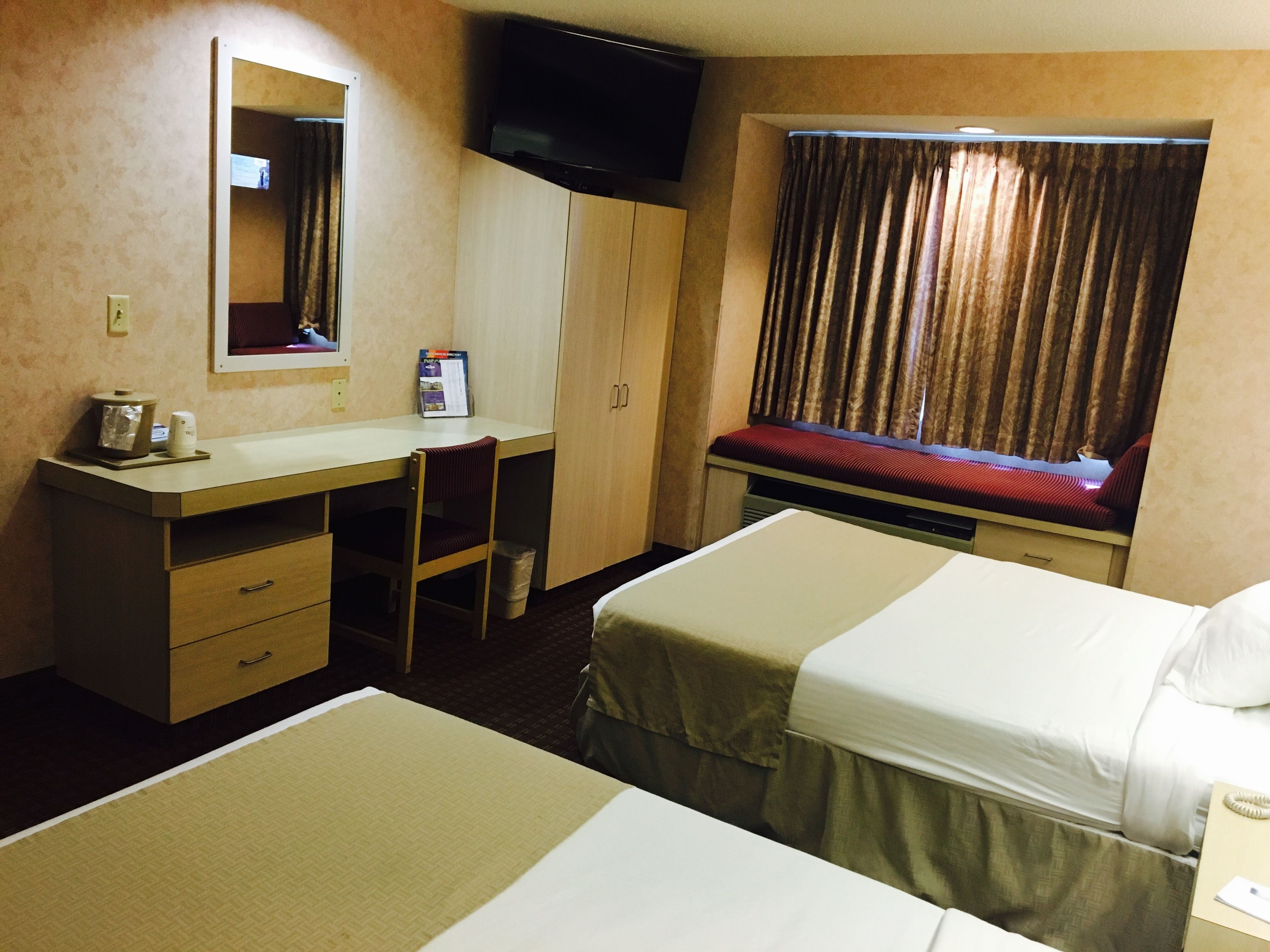 A hotel room with a desk, two beds, a television, and a window with curtains.