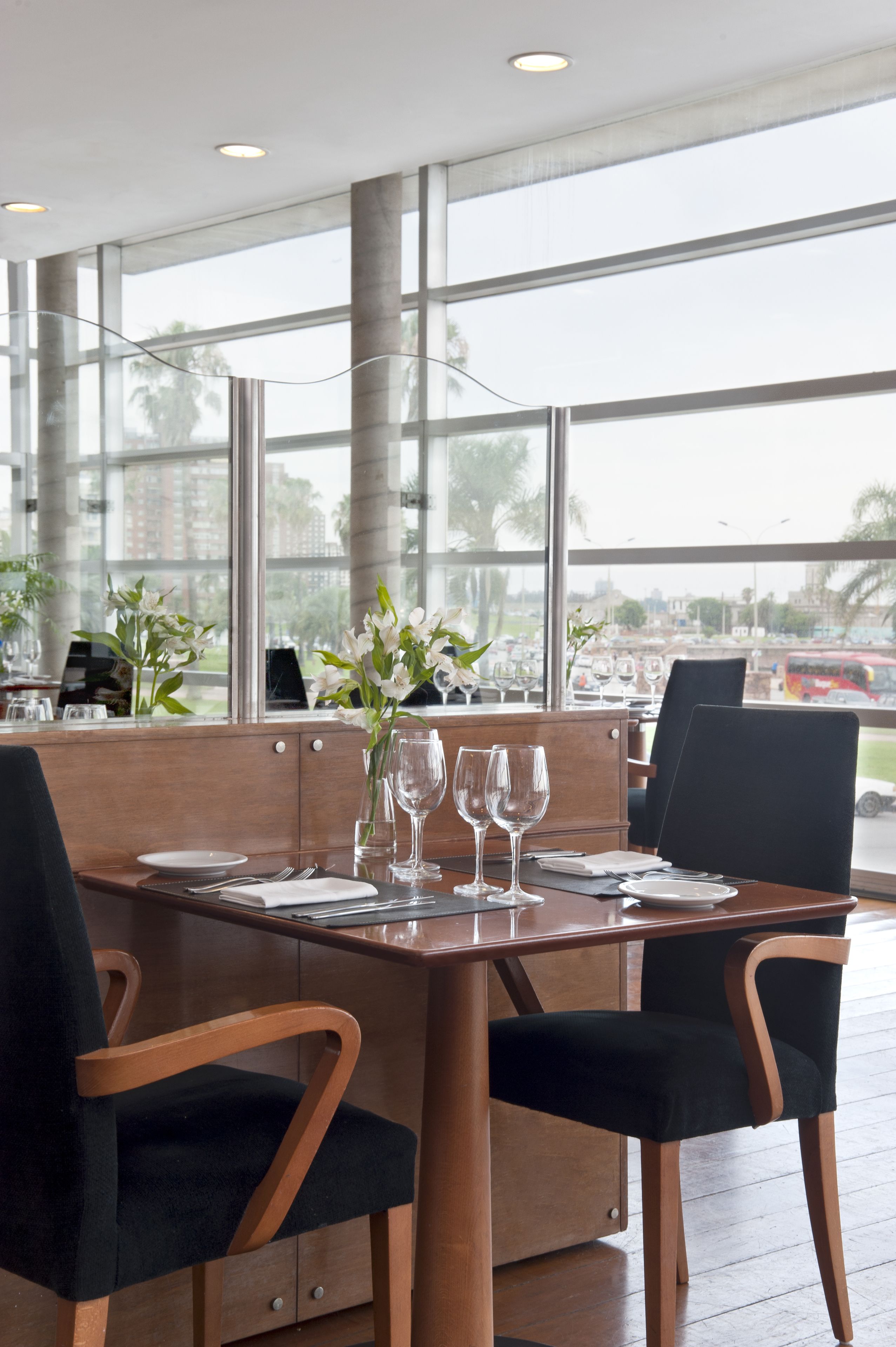 A dining area with a wooden table set for two, large windows, and a view of the cityscape.