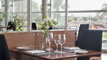 A dining area with a wooden table set for two, large windows, and a view of the cityscape.