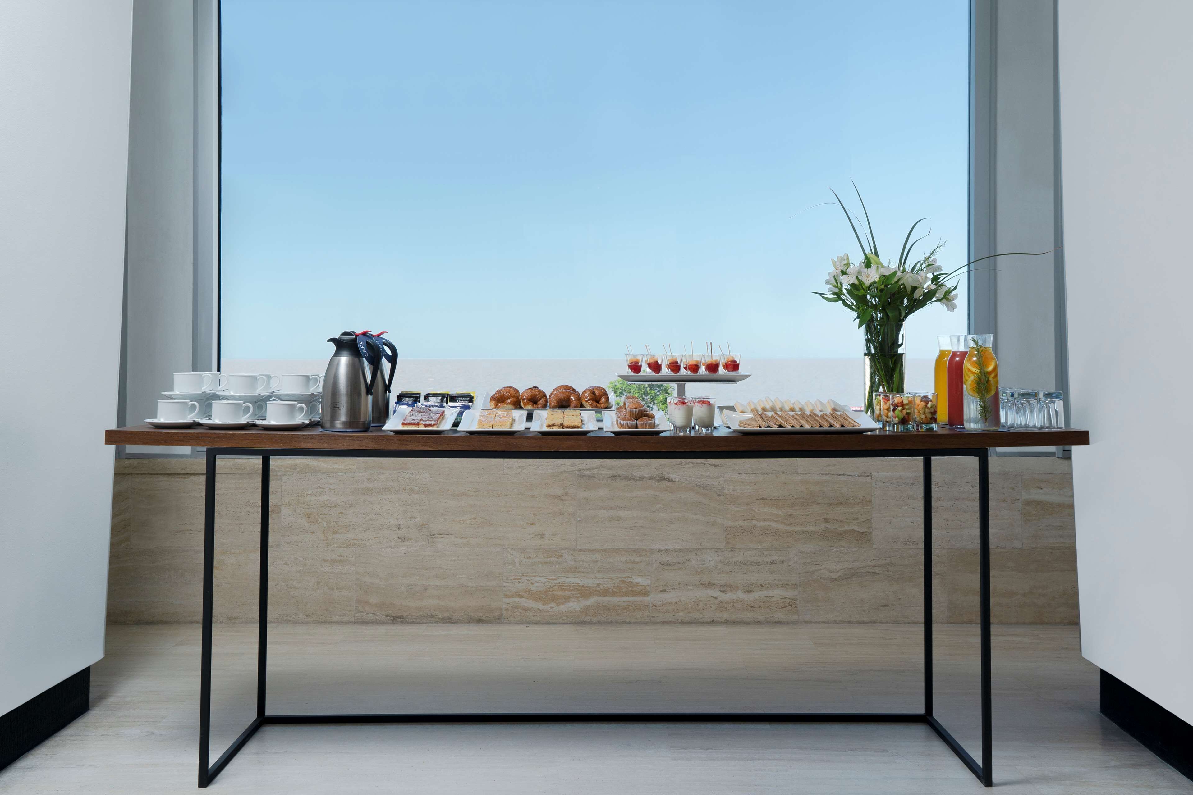 A breakfast buffet table with various food items and a coffee pot, set against a large window with a clear view.