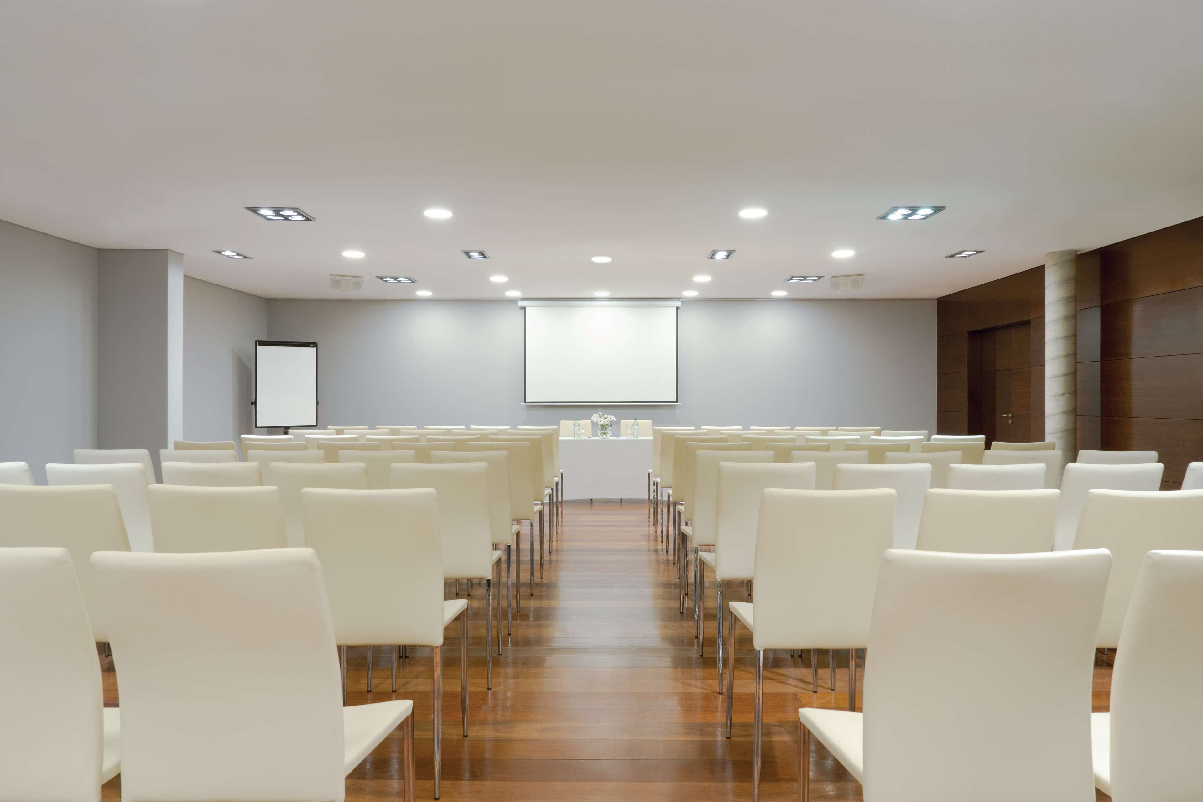 Un salón de conferencias con filas de sillas blancas, un atril y una pantalla de proyector.