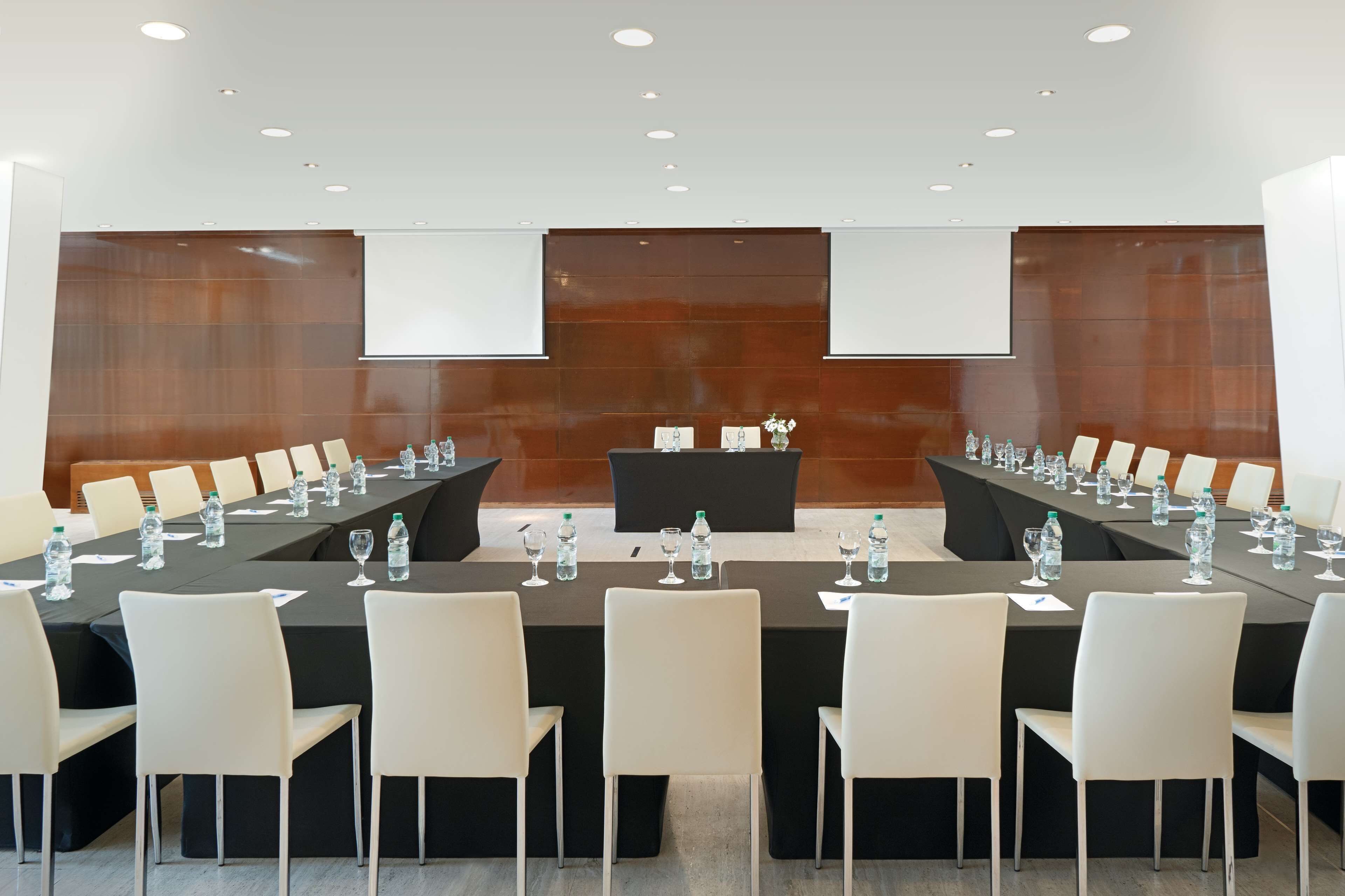 A conference room with a long table, white chairs, water bottles, and a podium.