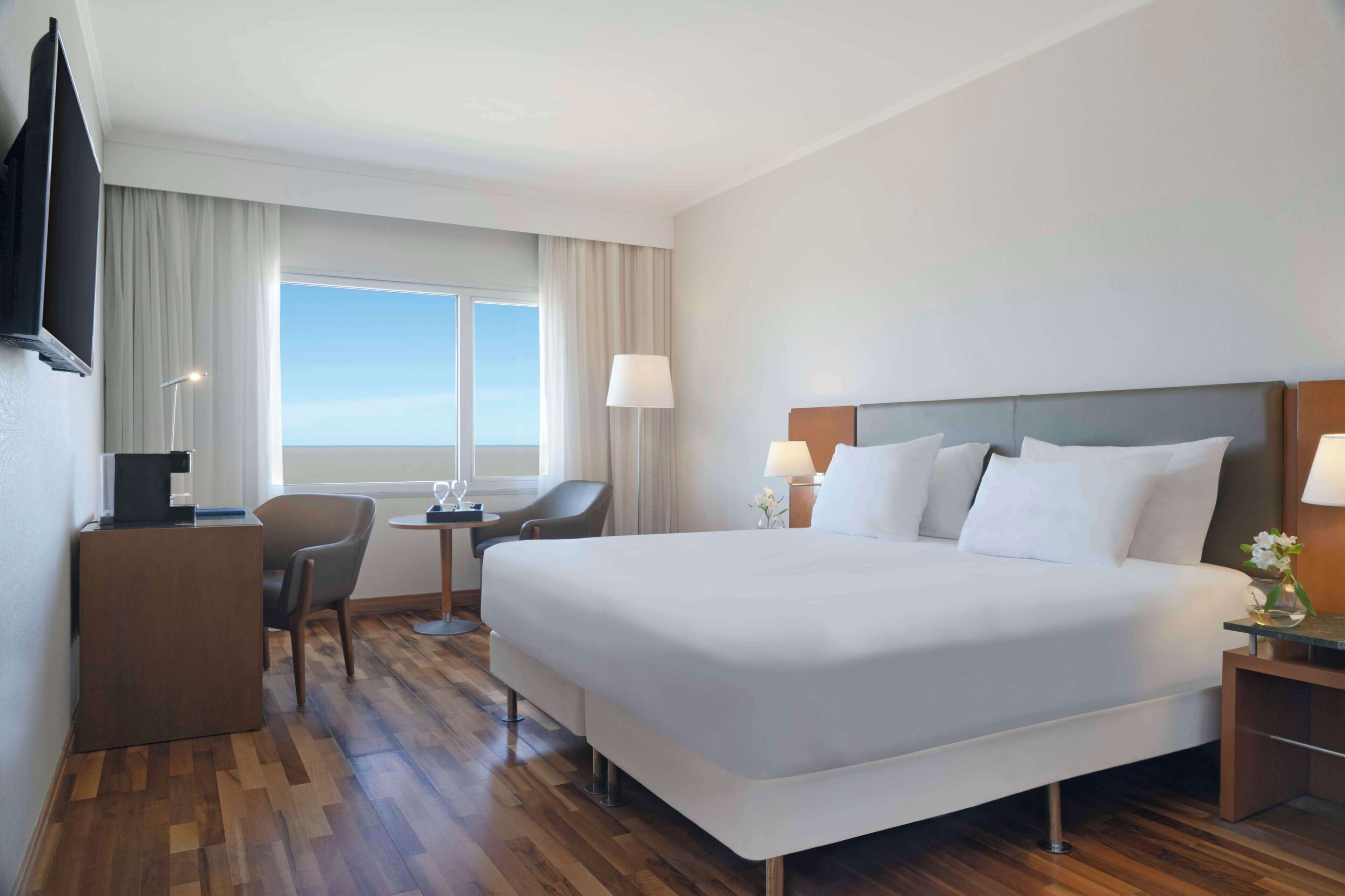 A hotel room with a large bed, a desk, a chair, a TV, and a window with curtains.