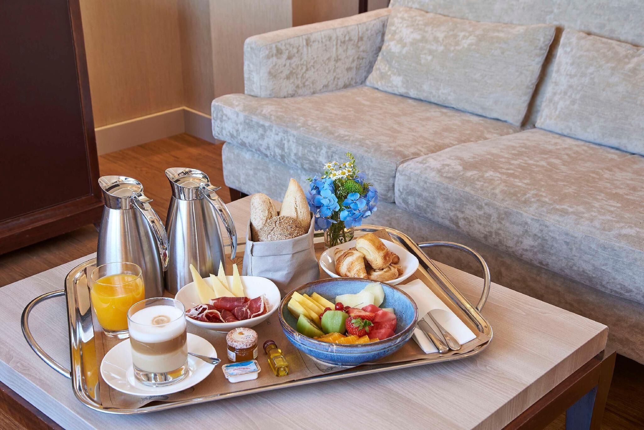 A breakfast tray with various food items and drinks on a tray, placed on a table in front of a sofa.