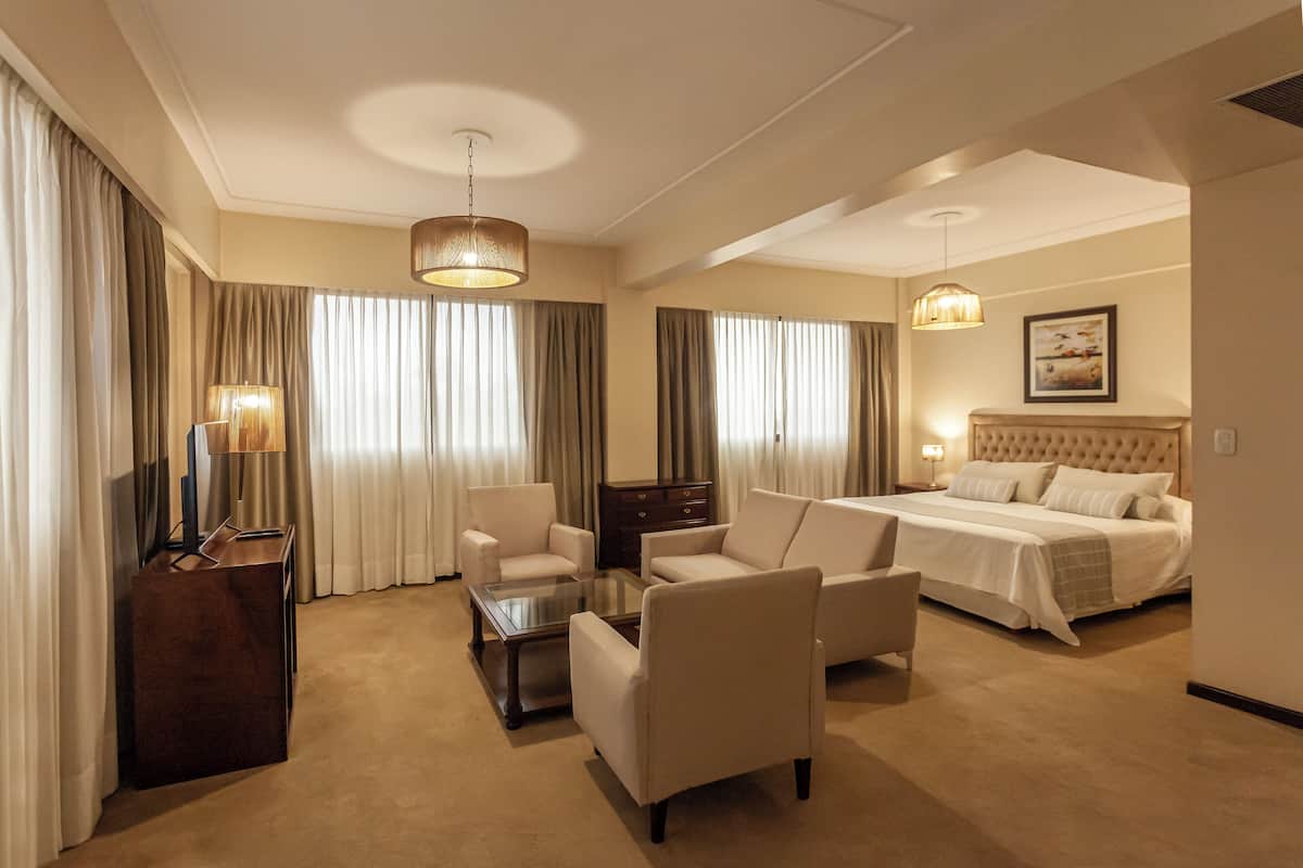 Ein Hotelzimmer mit einem großen Bett, zwei Sesseln, einem Couchtisch, einem Schreibtisch und einem Fernseher.