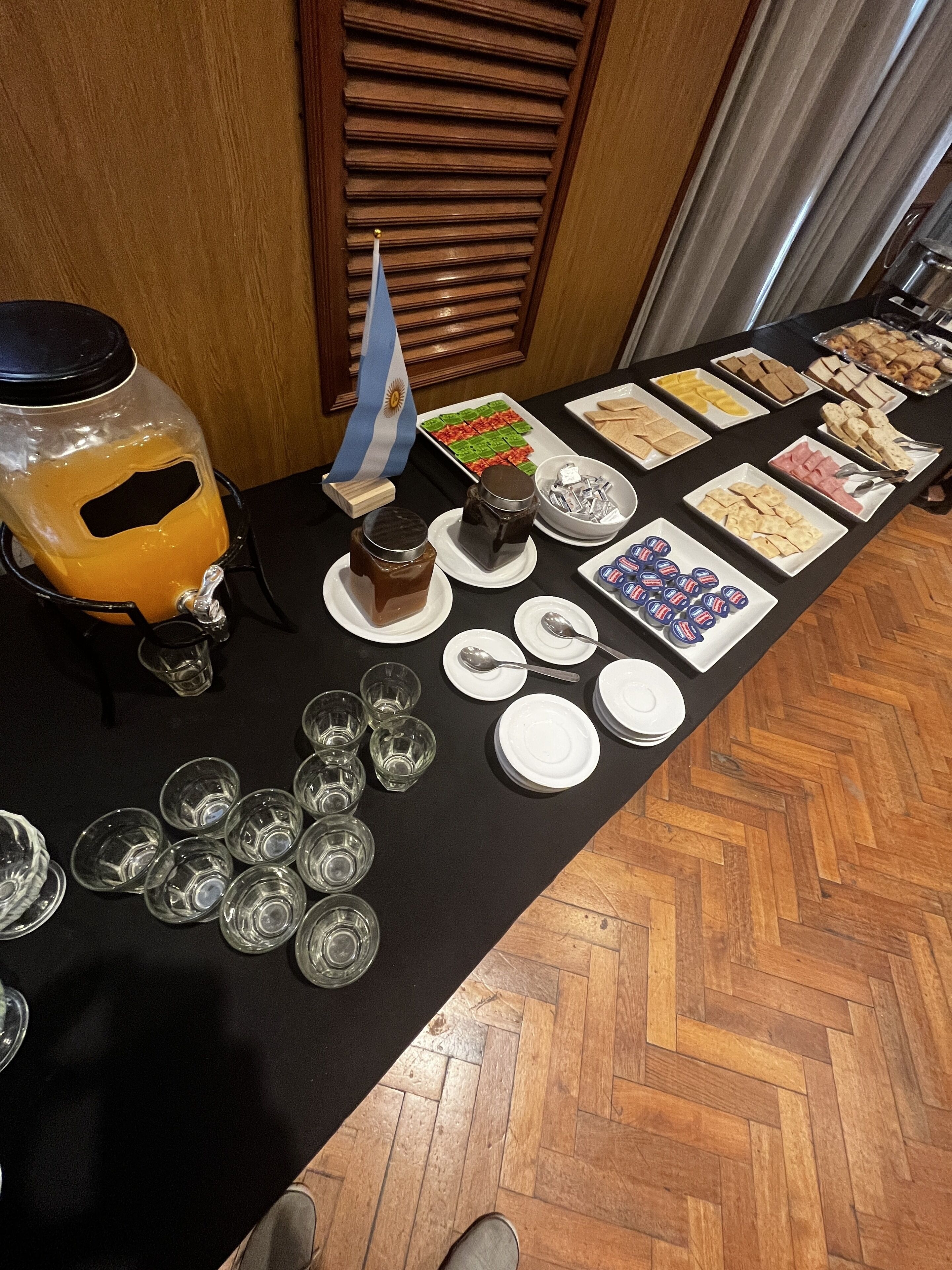 A buffet table with various food items and beverages, including a flag, plates, and glasses.