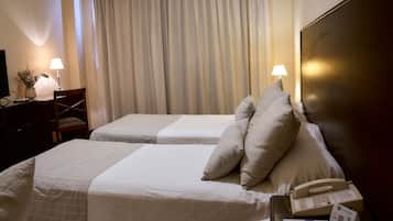 A hotel room with two beds, a desk with a lamp, a telephone, and a vase with flowers.