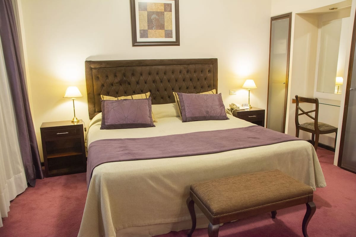 Ein Hotelzimmer mit einem großen Bett, zwei Nachttischen mit Lampen, einem Sessel und einem Spiegel.