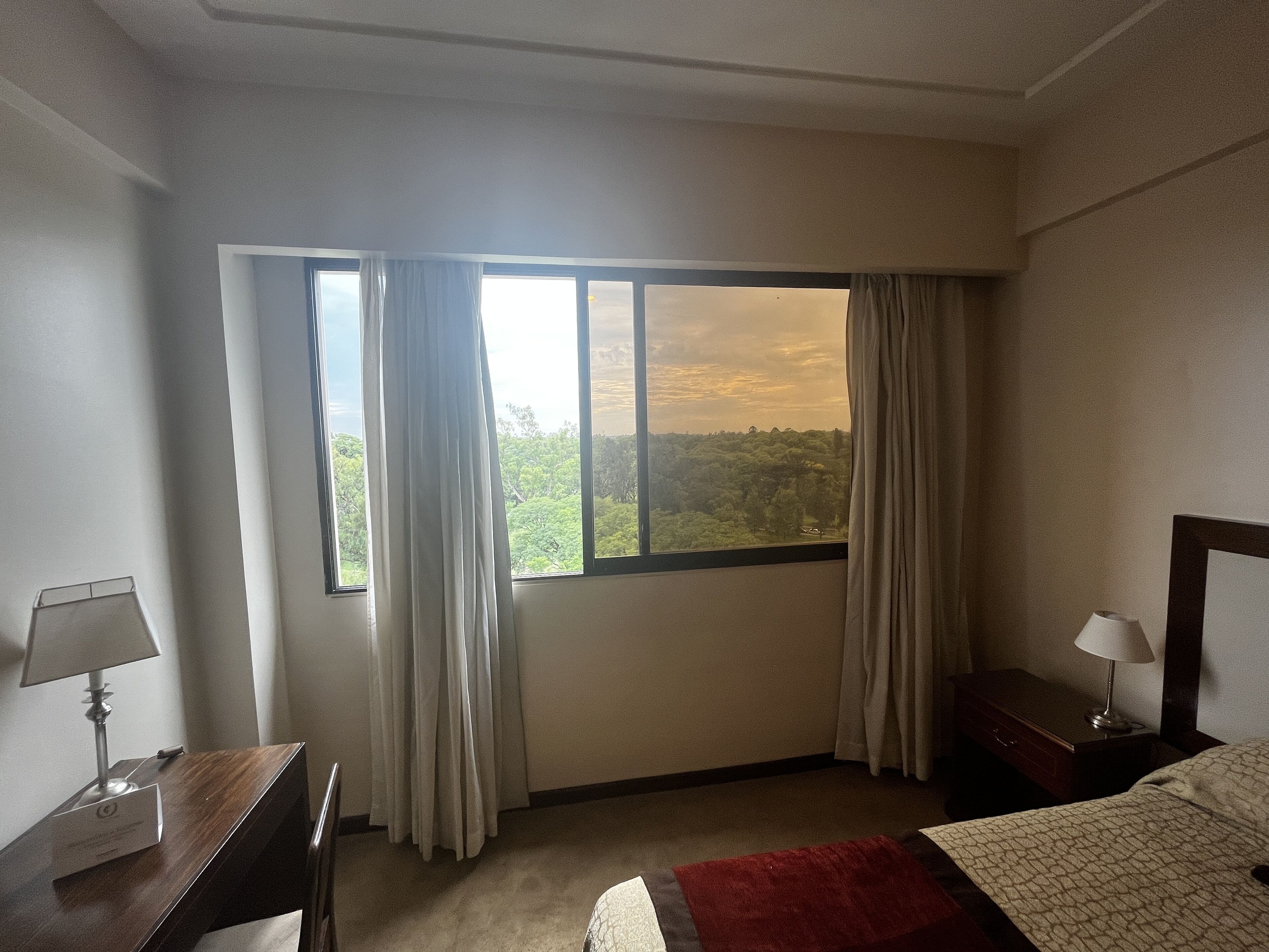 Habitación de hotel con un ventanal grande, una cama, una mesita de noche con lámpara y una silla.