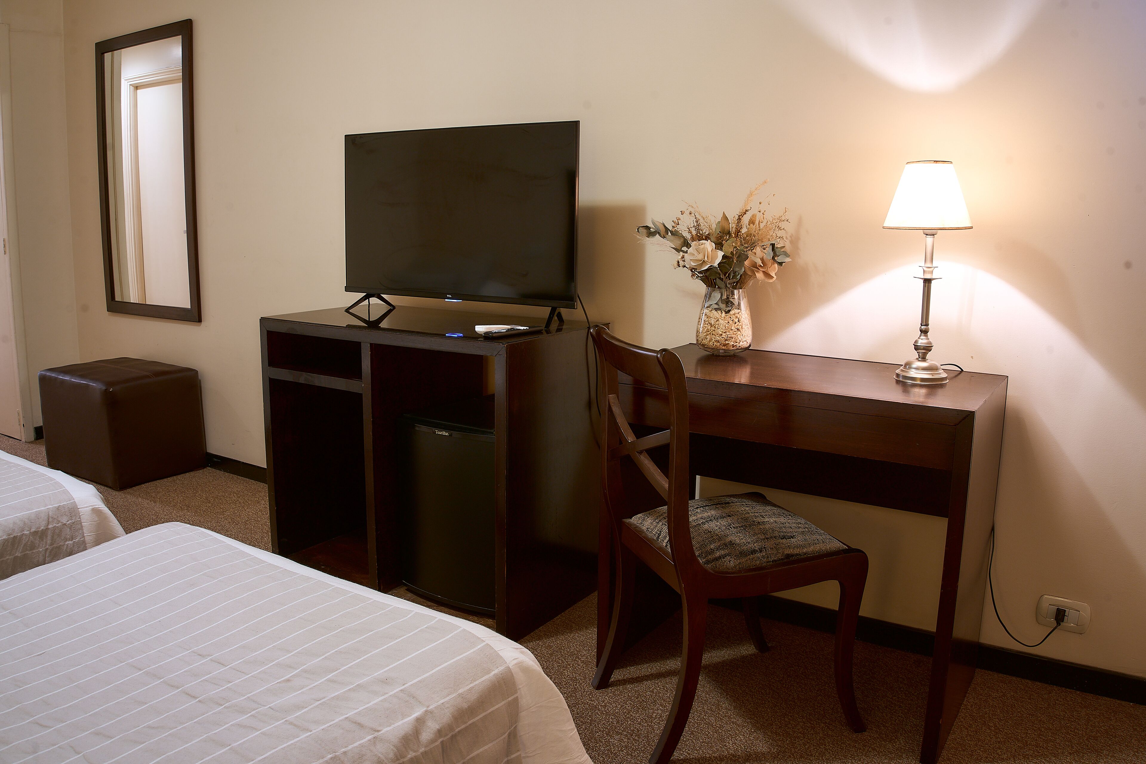 Habitación de hotel con una cama, un escritorio con computadora, una silla, un televisor y una lámpara.