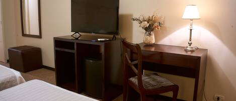 Habitación de hotel con una cama, un escritorio con computadora, una silla, un televisor y una lámpara.