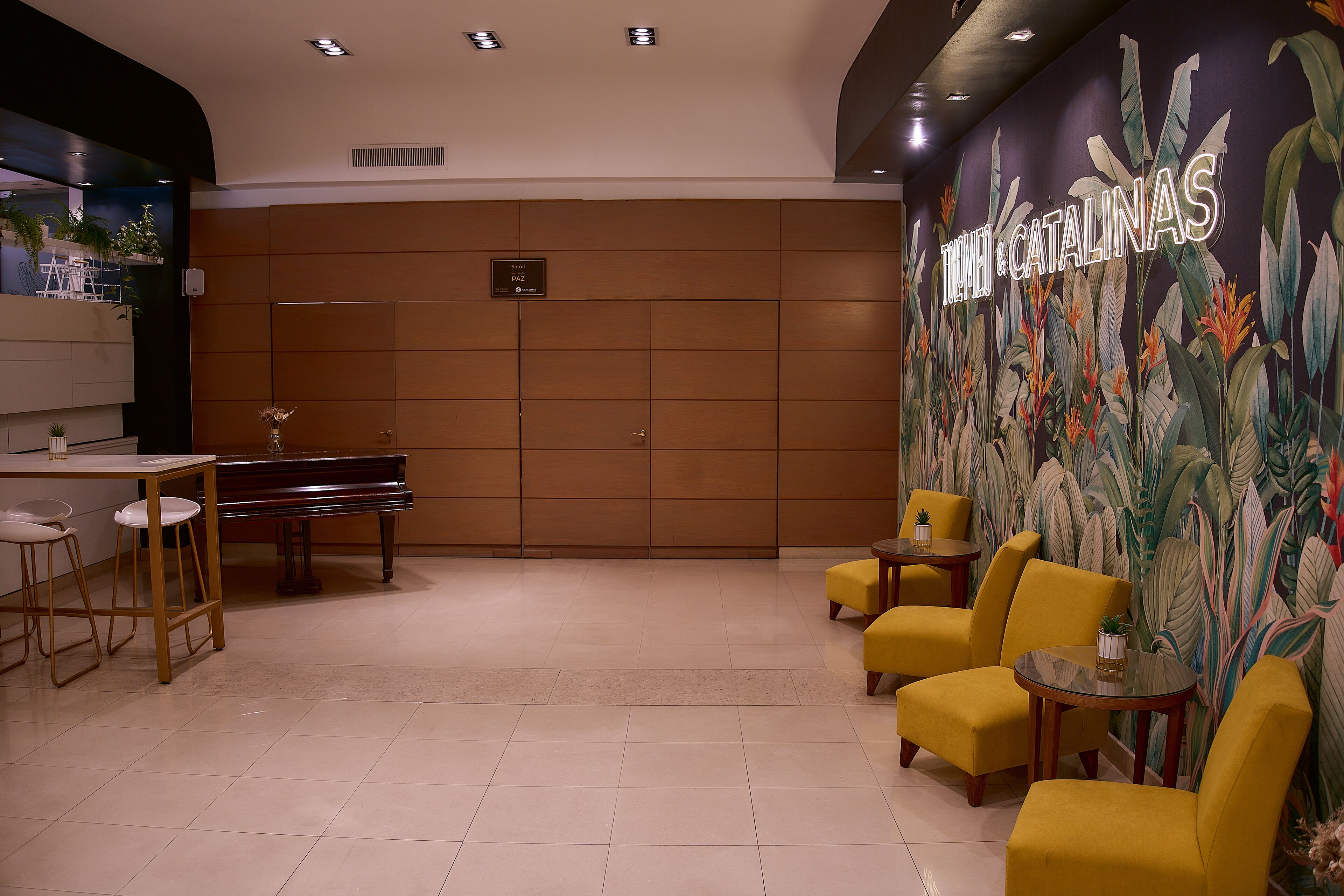 A lobby with a piano, yellow chairs, a table, and a wall mural.