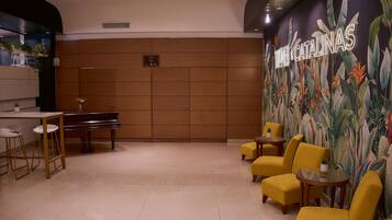 A lobby with a piano, yellow chairs, a table, and a wall mural.