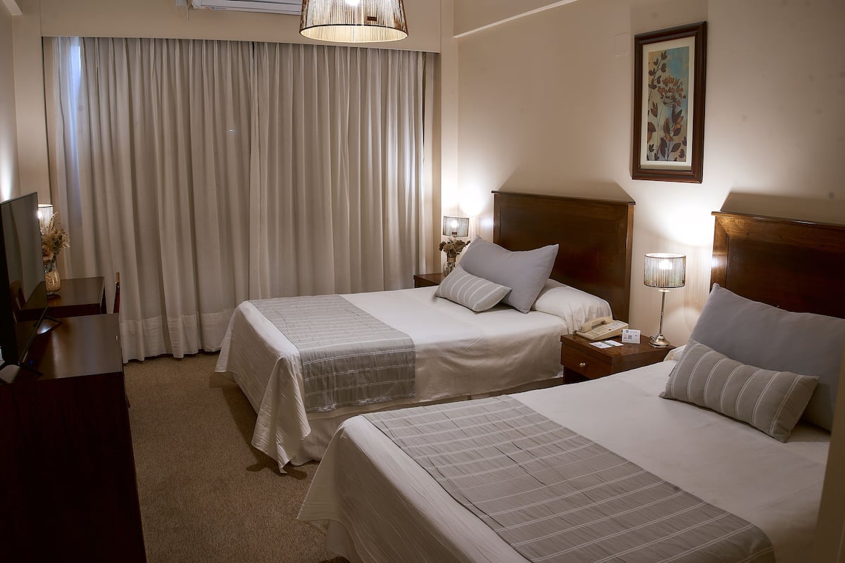 Ein Hotelzimmer mit zwei Betten, einem Schreibtisch, einem Stuhl, einer Lampe und einem Bild an der Wand.