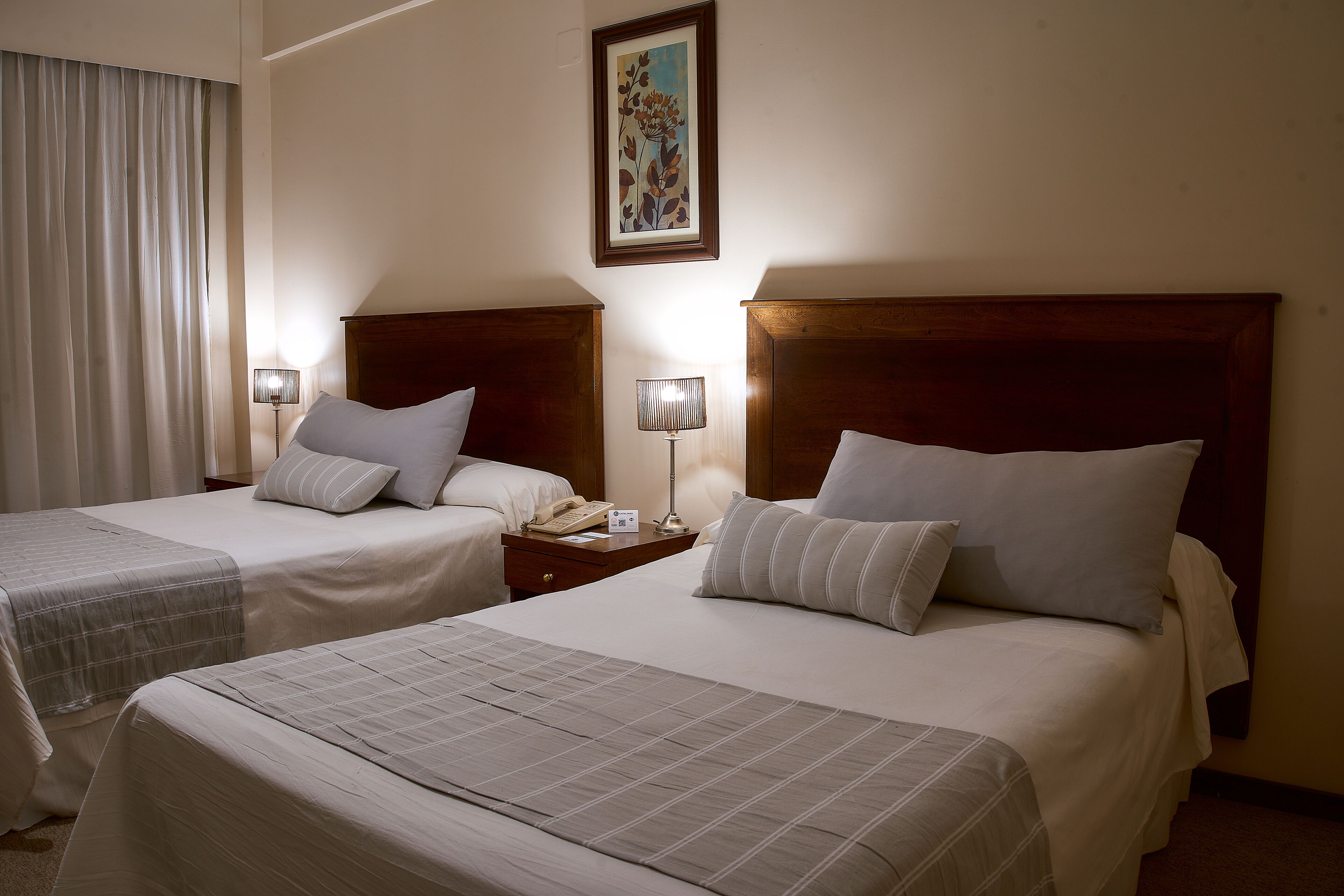 Una habitación de hotel con dos camas, una mesita de noche con lámpara y un cuadro en la pared.