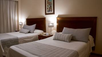 Una habitación de hotel con dos camas, una mesita de noche con lámpara y un cuadro en la pared.