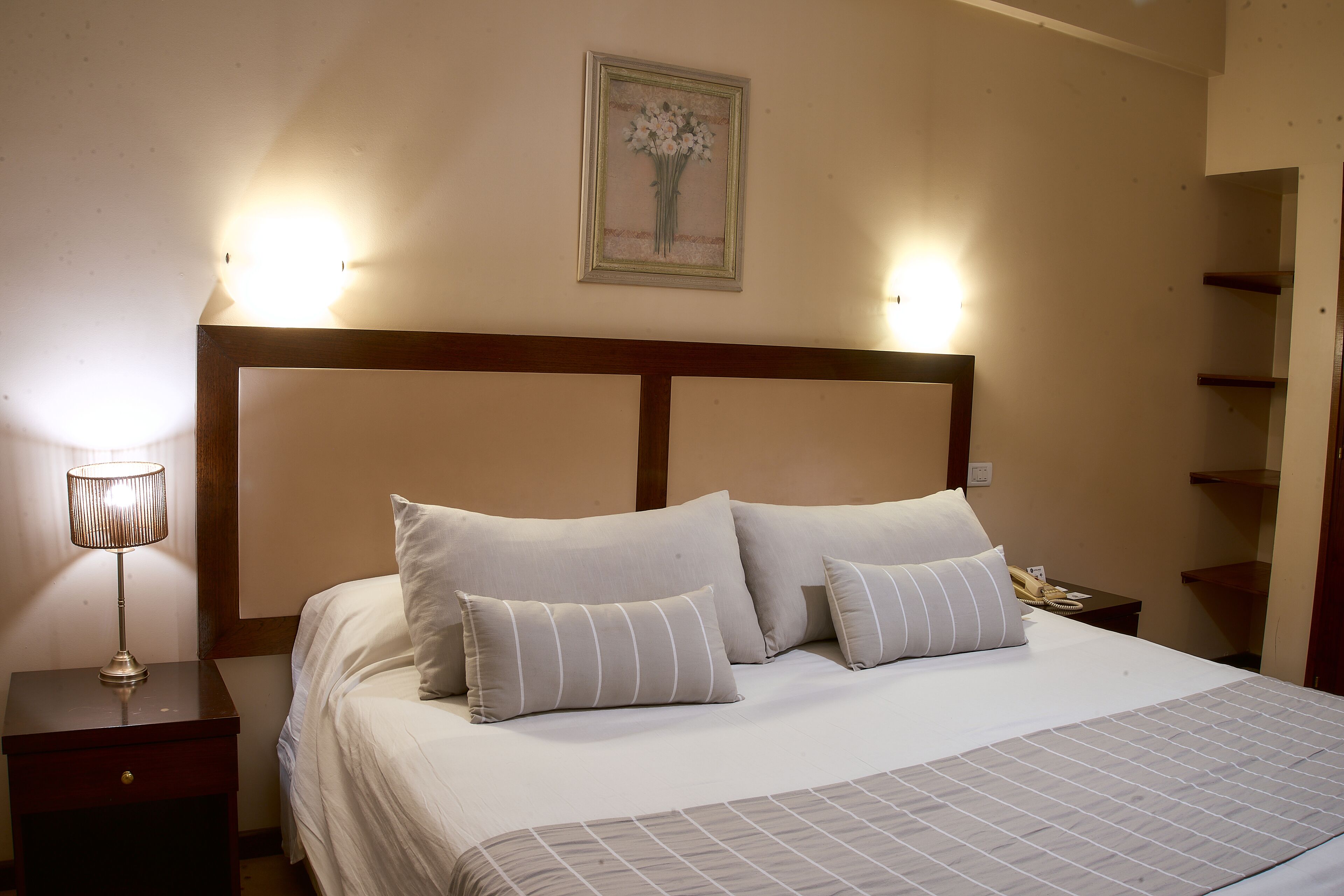 A neatly made bed with a headboard, a bedside lamp, and a framed picture on the wall.