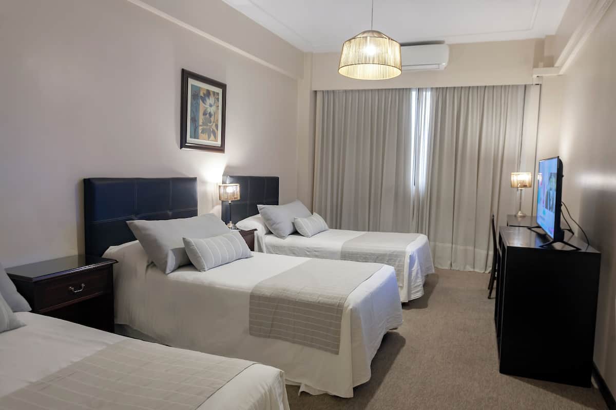 Ein Hotelzimmer mit zwei Betten, einem Schreibtisch, einem Fernseher und einem großen Fenster mit Vorhängen.