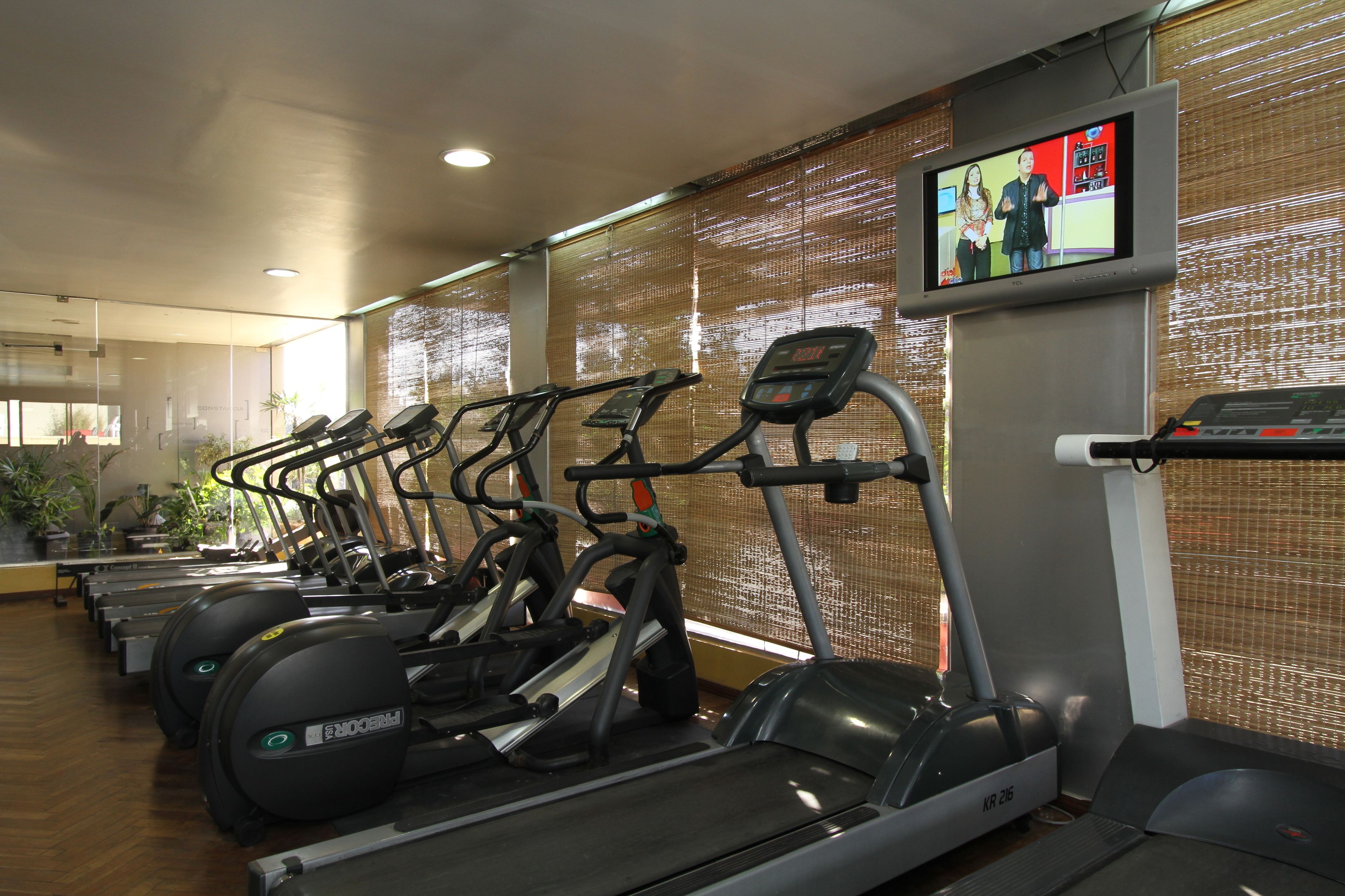 A row of treadmills in a gym with a television screen displaying a show.