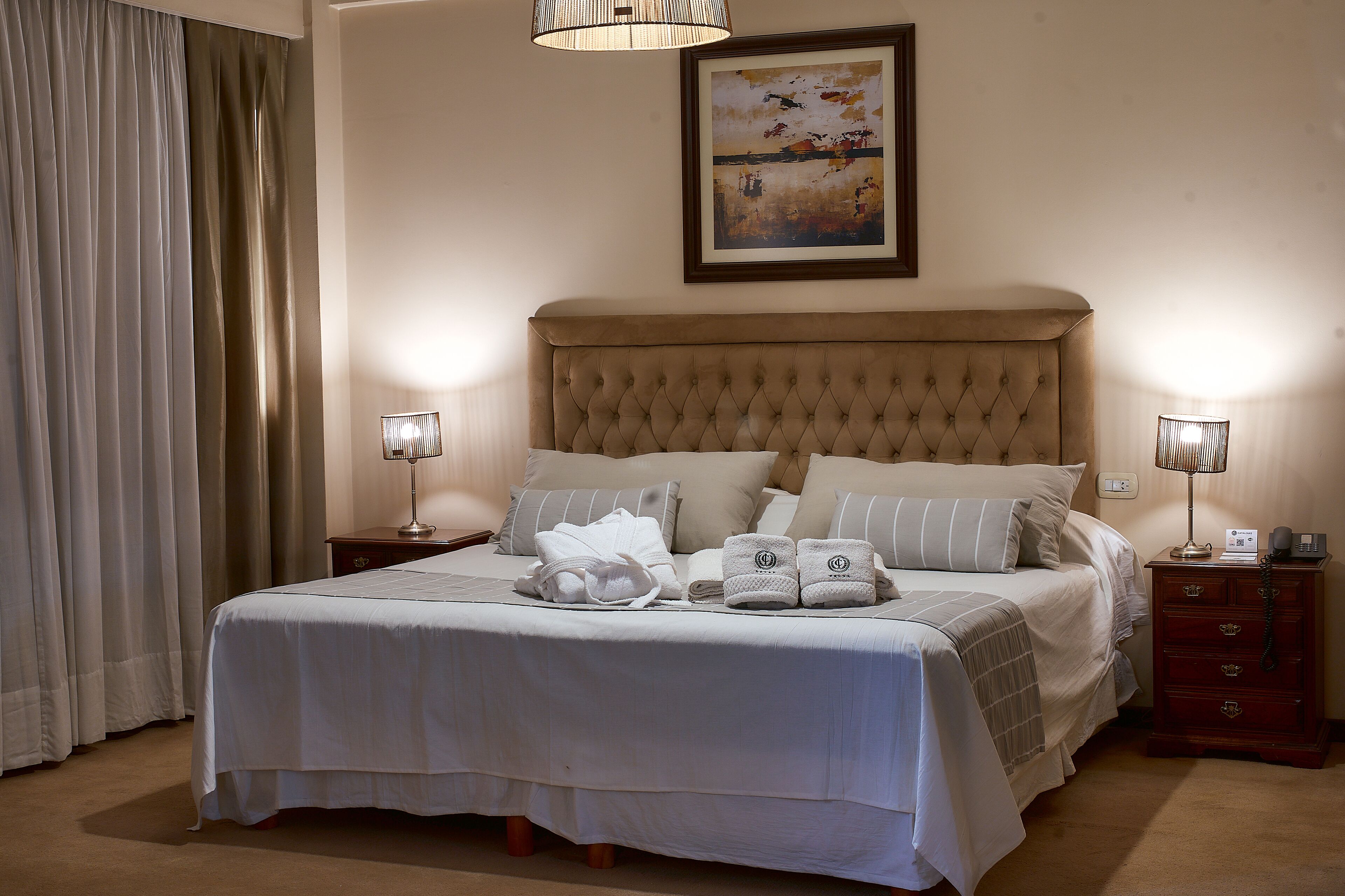 A neatly made bed with a headboard, two bedside tables with lamps, and a painting on the wall.