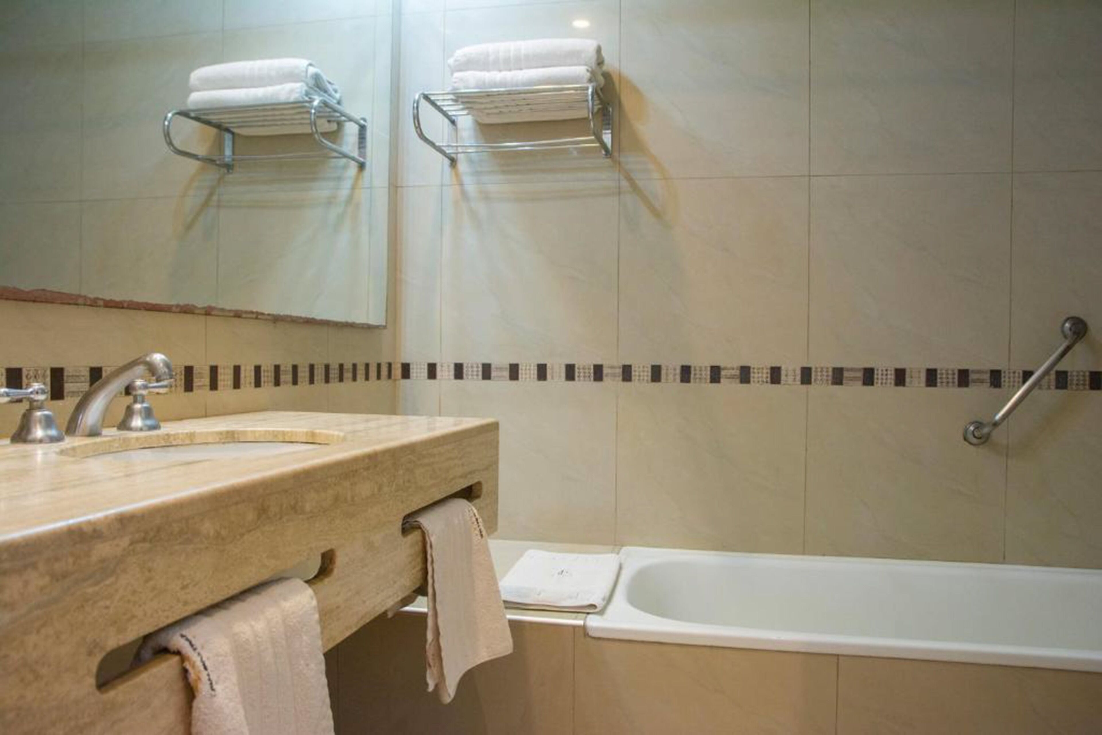 Ein Badezimmer mit Marmorwaschbecken, einem Spiegel, einem Handtuchhalter mit zwei Handtüchern, einer Badewanne und einer Haltestange.