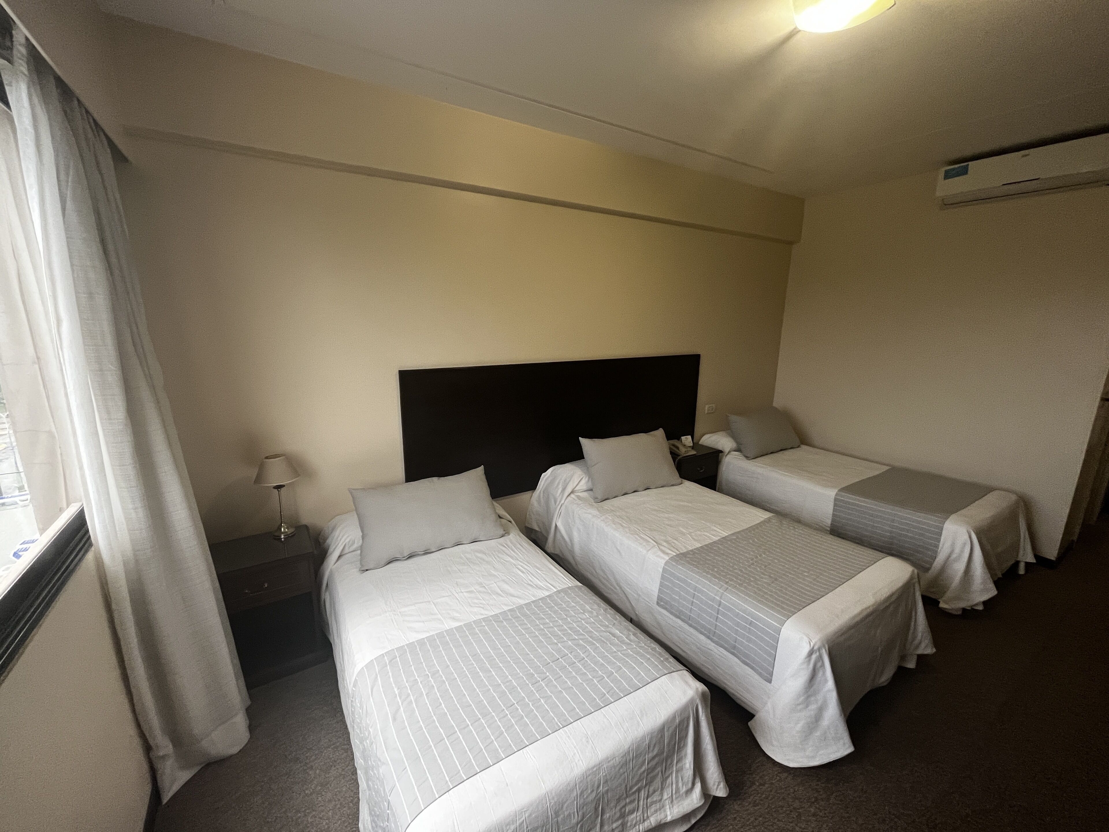 Une chambre d’hôtel avec deux lits simples, une table de chevet avec une lampe et une fenêtre avec des rideaux.