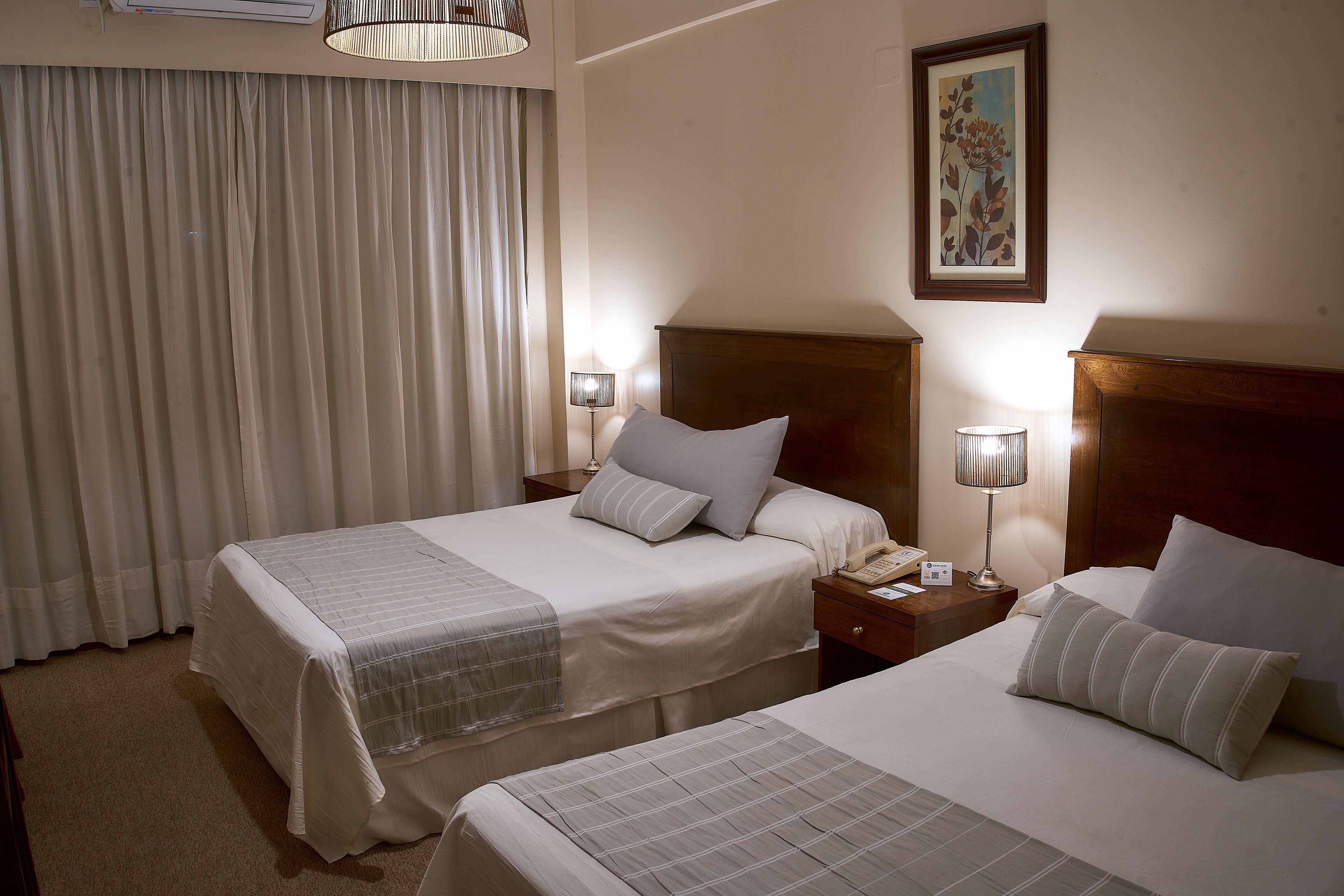 A hotel room with two beds, a nightstand with a lamp, and a painting on the wall.