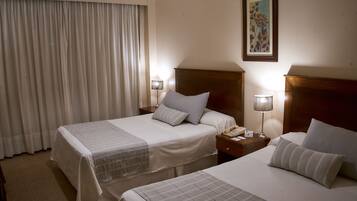 A hotel room with two beds, a nightstand with a lamp, and a painting on the wall.