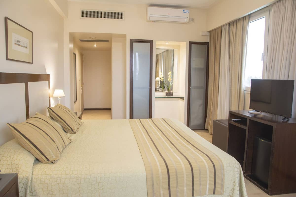 Ein Hotelzimmer mit Bett, Fernseher, Schreibtisch und einem Fenster mit Vorhängen.