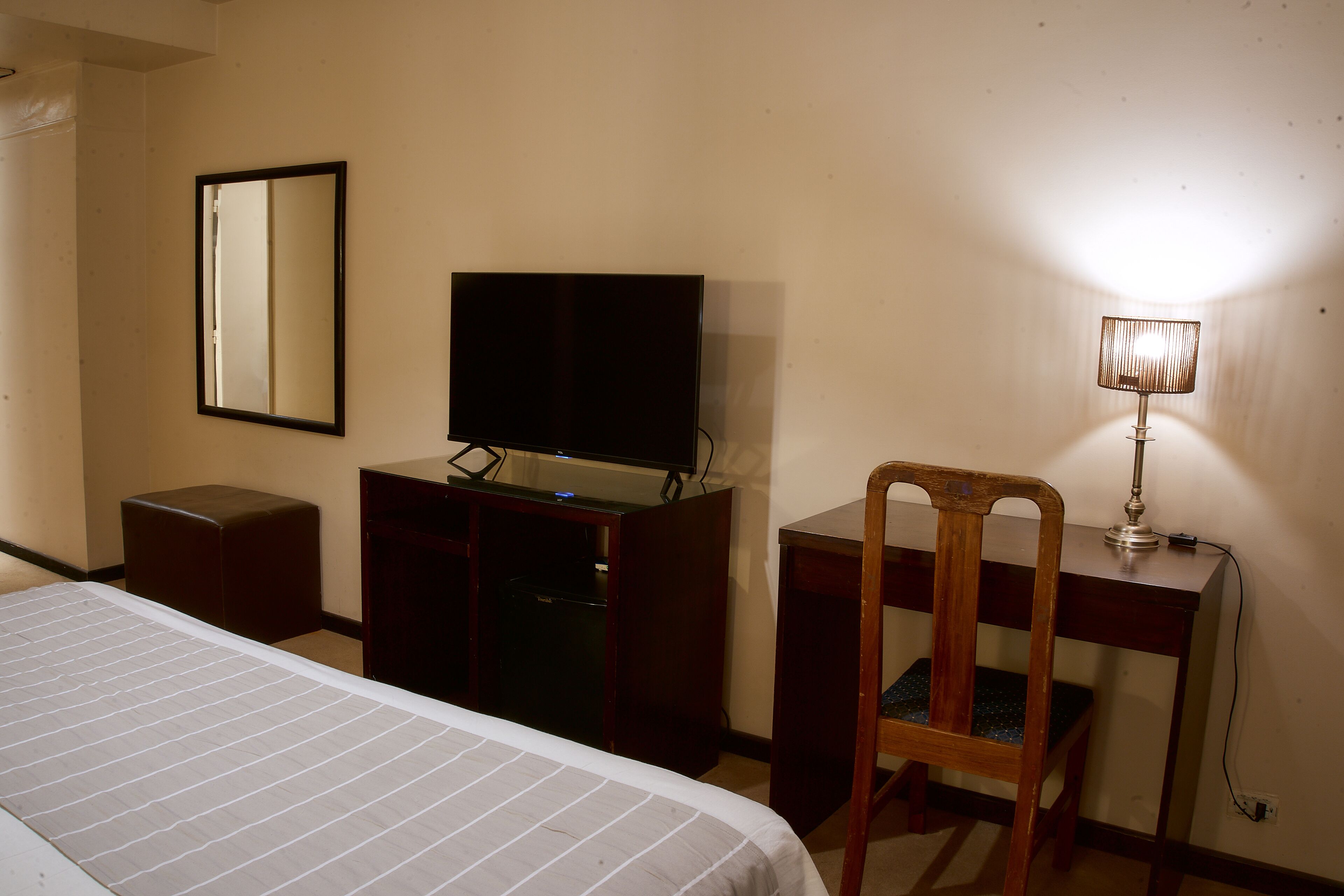 Une chambre d’hôtel comprenant un lit, un bureau avec une télévision, une chaise et une lampe.
