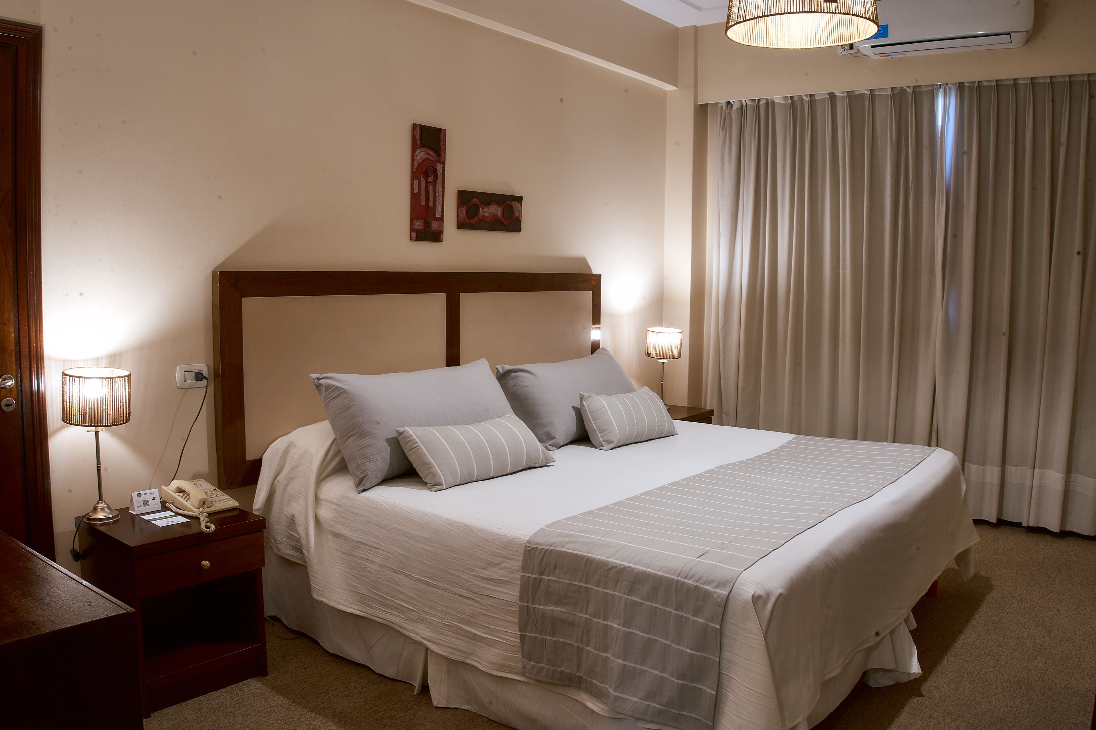A neatly made bed with a headboard, a bedside table with a lamp, and a wall-mounted air conditioner.