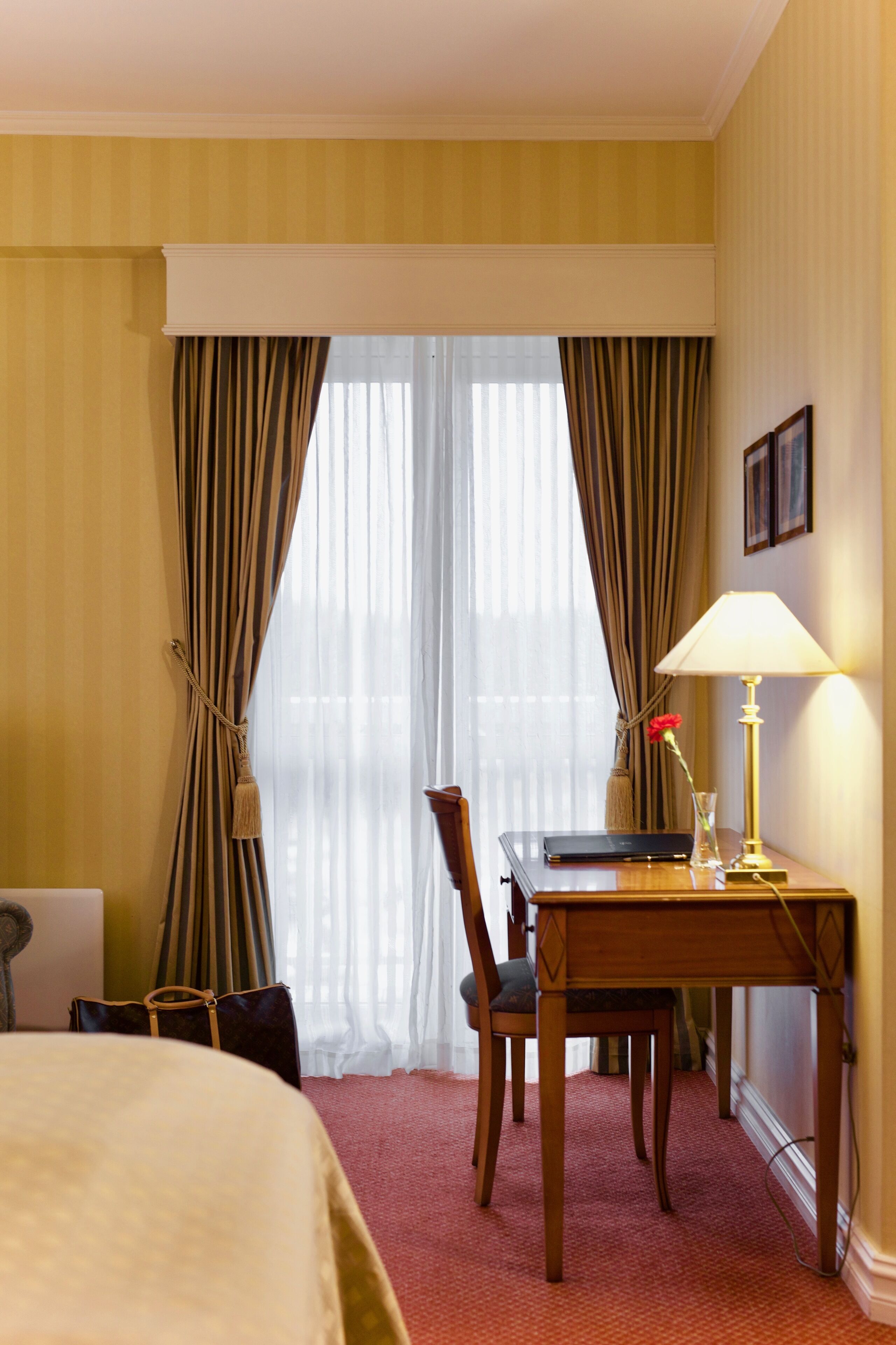 Habitación de hotel con una cama, un escritorio con lámpara, una silla y una ventana con cortinas.