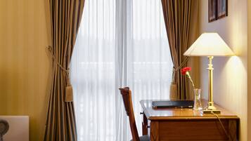 Habitación de hotel con una cama, un escritorio con lámpara, una silla y una ventana con cortinas.