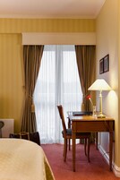 Habitación de hotel con una cama, un escritorio con lámpara, una silla y una ventana con cortinas.