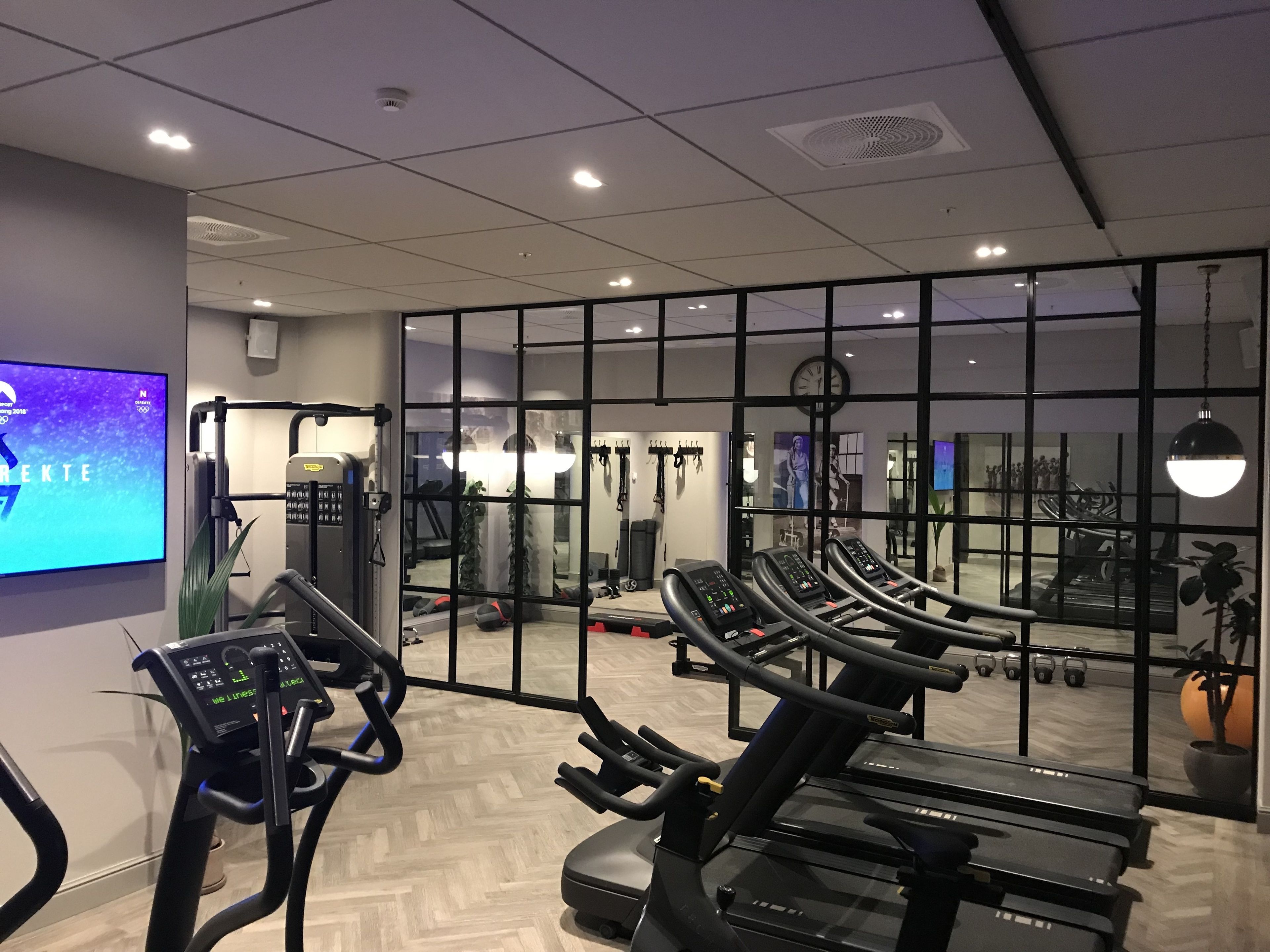 Et træningscenter med løbebånd, styrkemaskiner og et spejl.