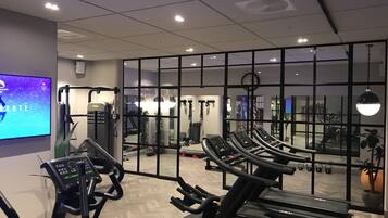 Un gimnasio con cintas de correr, máquinas de pesas y un espejo grande.