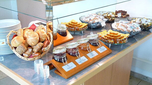 Buffet com diversos alimentos, incluindo pães, bolos e geleias.