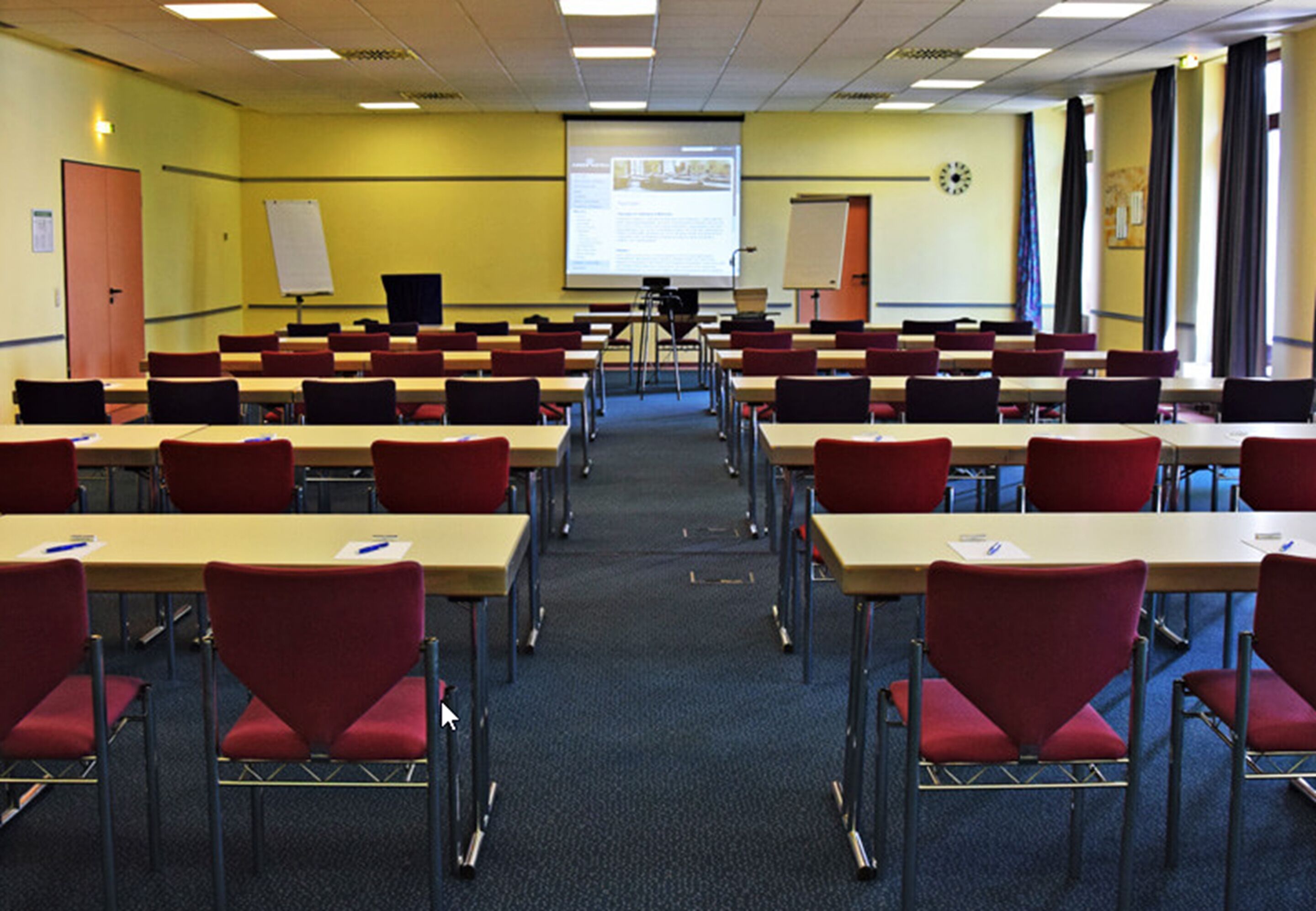 A classroom with rows of desks and chairs, a projector screen, and a whiteboard.