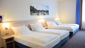 Quarto de hotel com duas camas, uma mesinha de cabeceira, um abajur fixado na parede e um quadro de um parque.