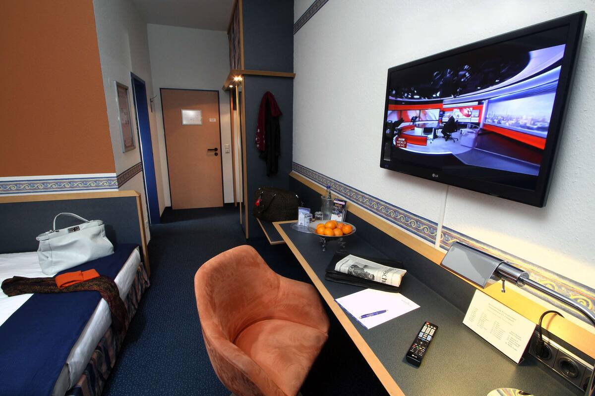 Habitación de hotel con una cama, un escritorio con televisor, una silla y una mesita con un tazón de naranjas y un control remoto.