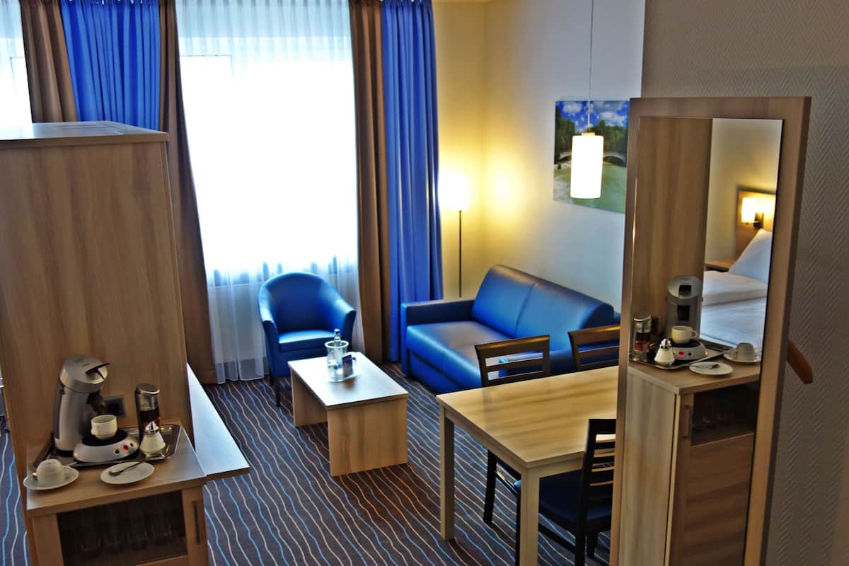 Habitación de hotel con cama, sofá, mesa de comedor, cafetera y televisor.