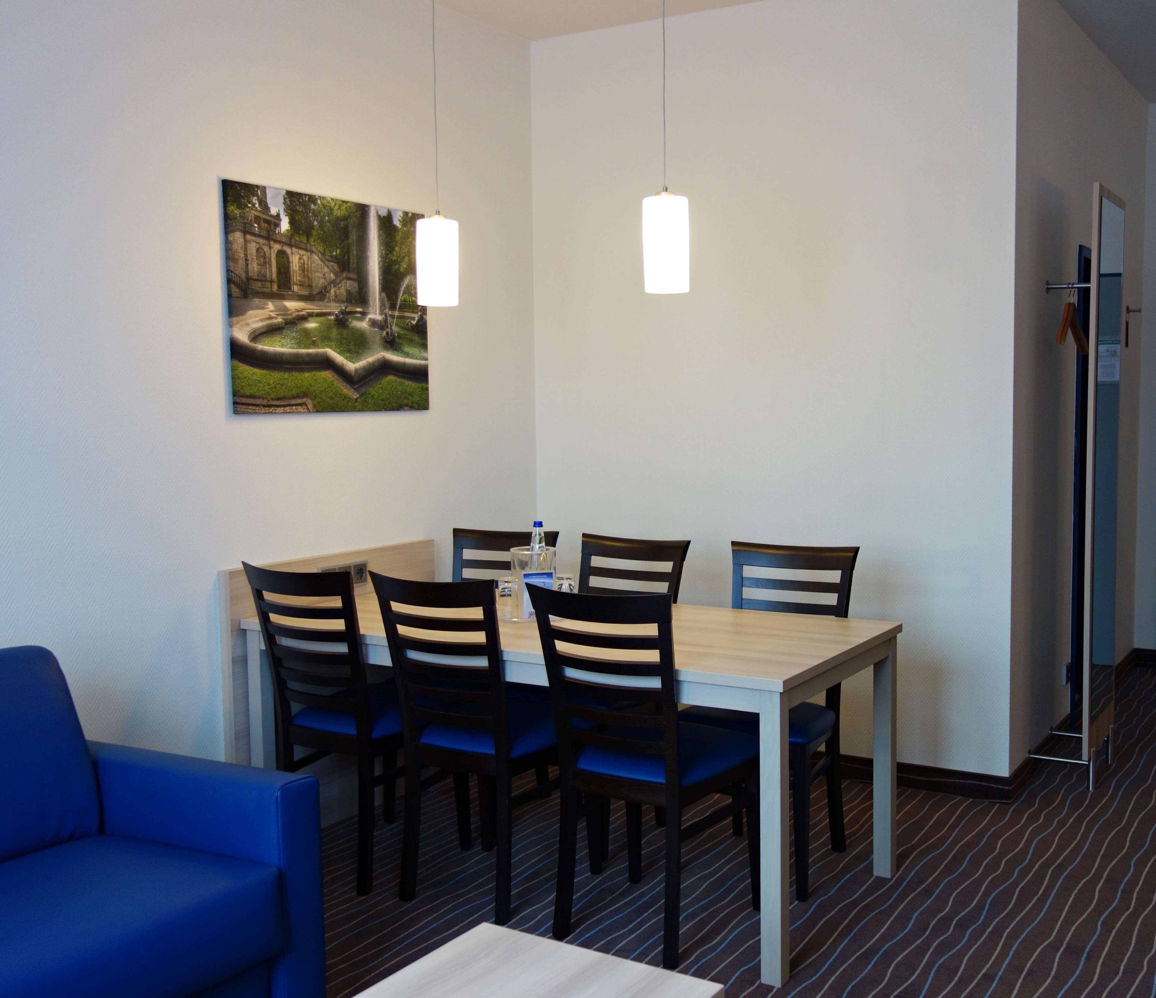 A dining area with a table and chairs, a blue sofa, and a painting on the wall.