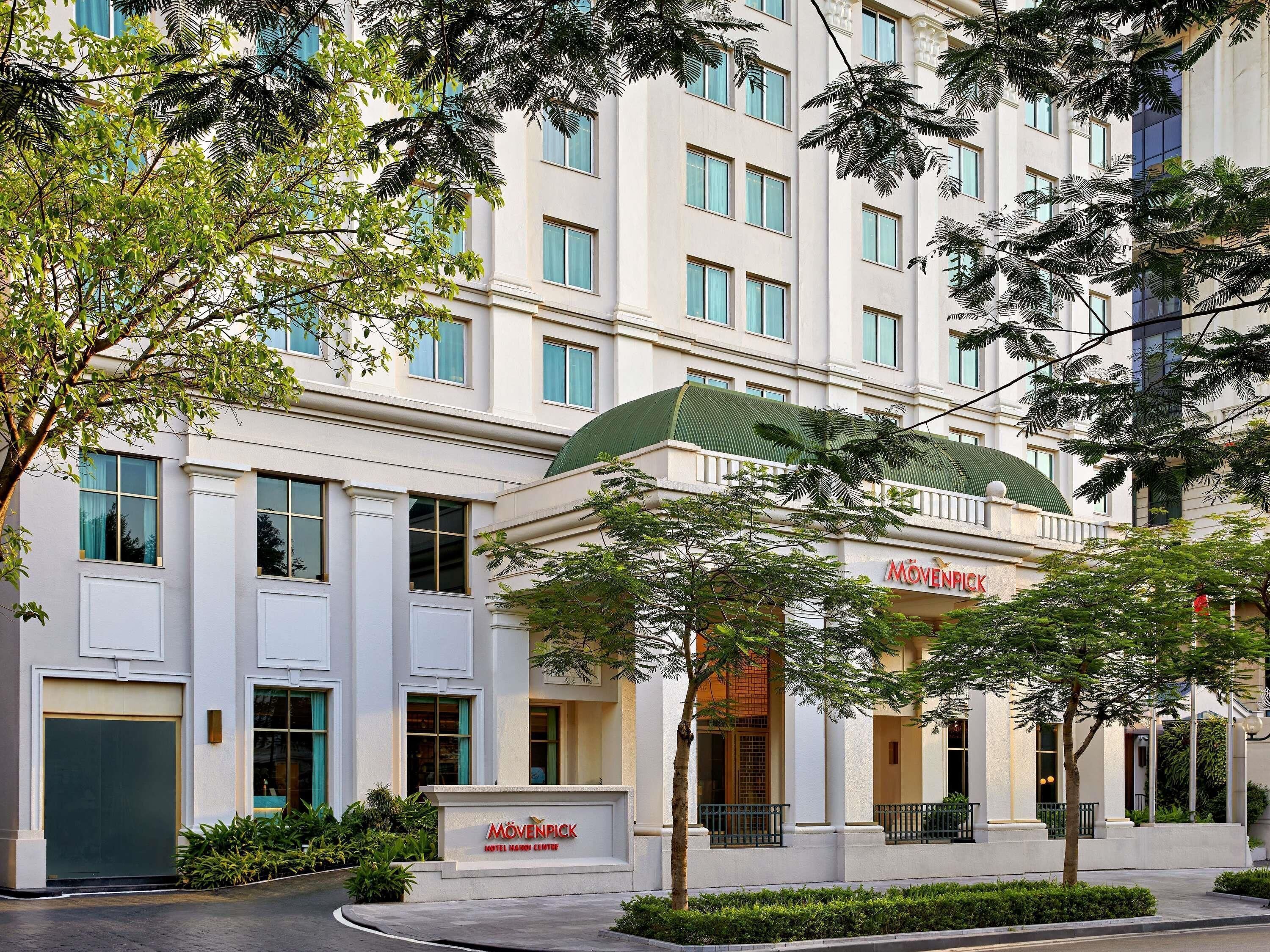 Un hotel de varios pisos con un llamativo toldo verde y un letrero que dice 'Mövenpick Hotel Hanoi Centre'.