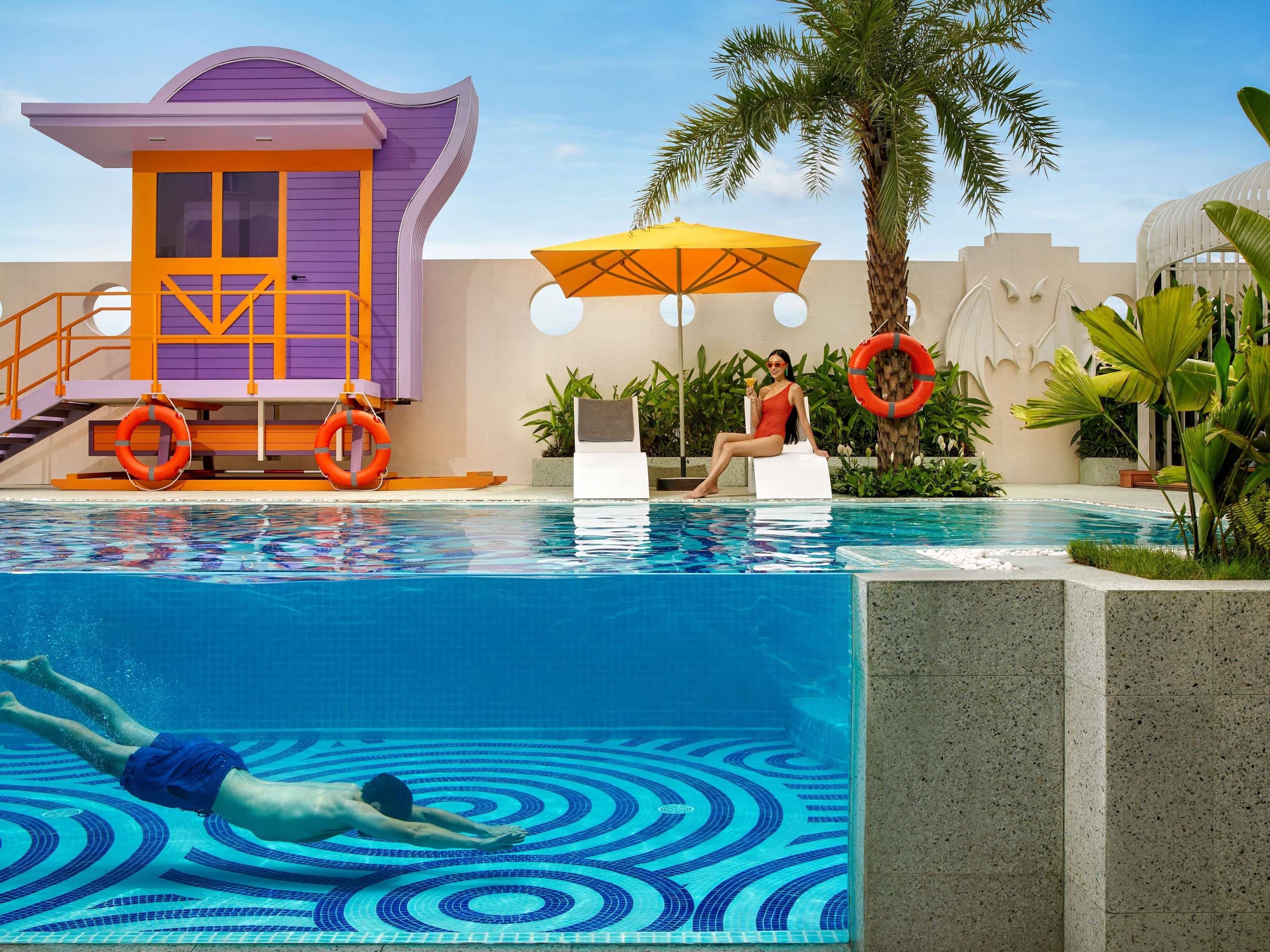 A swimming pool with a lifeguard tower, lounge chairs, and palm trees.